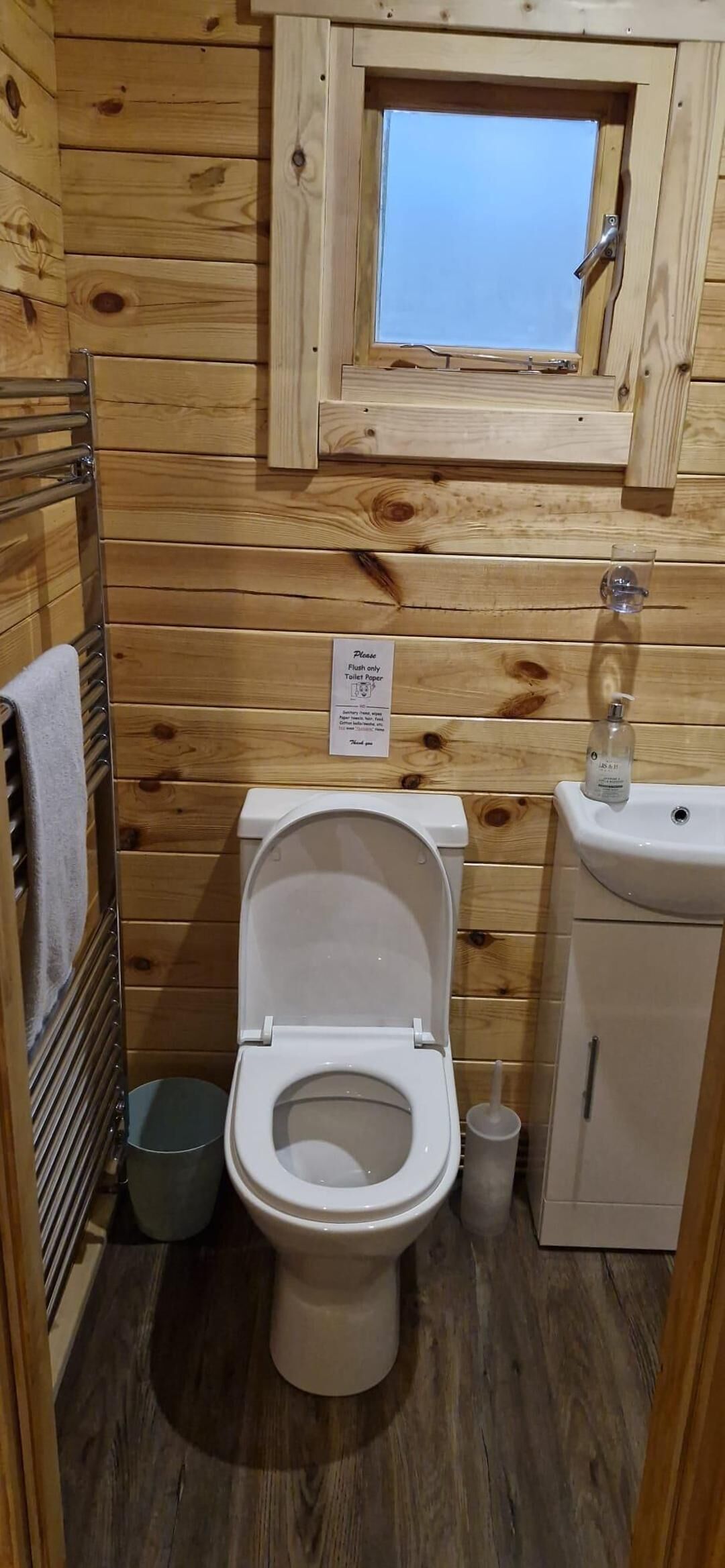 Un baño pequeño de madera con inodoro, lavamanos y una ventana sobre el inodoro.