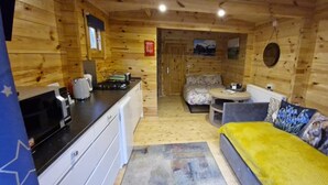 A wooden cabin interior with a kitchenette, a sofa with a blanket, and a dining area. - Birdsong Lodge Dog Friendly Nr Sutton on Sea (Mablethorpe)