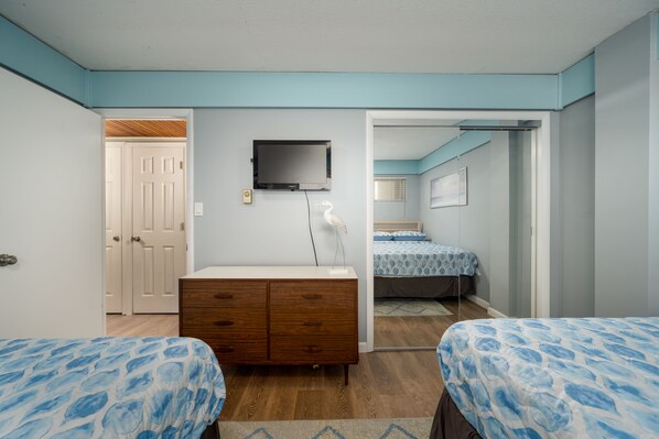 A bedroom with two beds, a dresser, a TV, and a door leading to another room. - Oceanfront condo - sunrise views, direct beach access & pool (Ocean City)