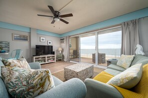 A living room with a TV, sofa, and a balcony with a view. - Oceanfront condo - sunrise views, direct beach access & pool (Ocean City)