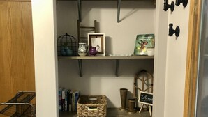 Un couloir étroit avec une porte en bois, un présentoir en métal et une étagère contenant des livres et un jeu de société.