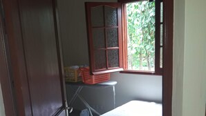 A room with a bed, a window with a view of greenery, a door, and a small table with baskets. - Villa of 100 m2 flower gardens and fruit trees (Le Moule)