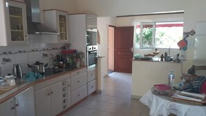A kitchen with cabinets, a stove, and a table with a tablecloth. - Villa of 100 m2 flower gardens and fruit trees (Le Moule)