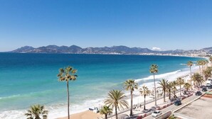 A coastal road with palm trees, a beach, and mountains in the background. - Waterfront - splendid apartment (Cannes)