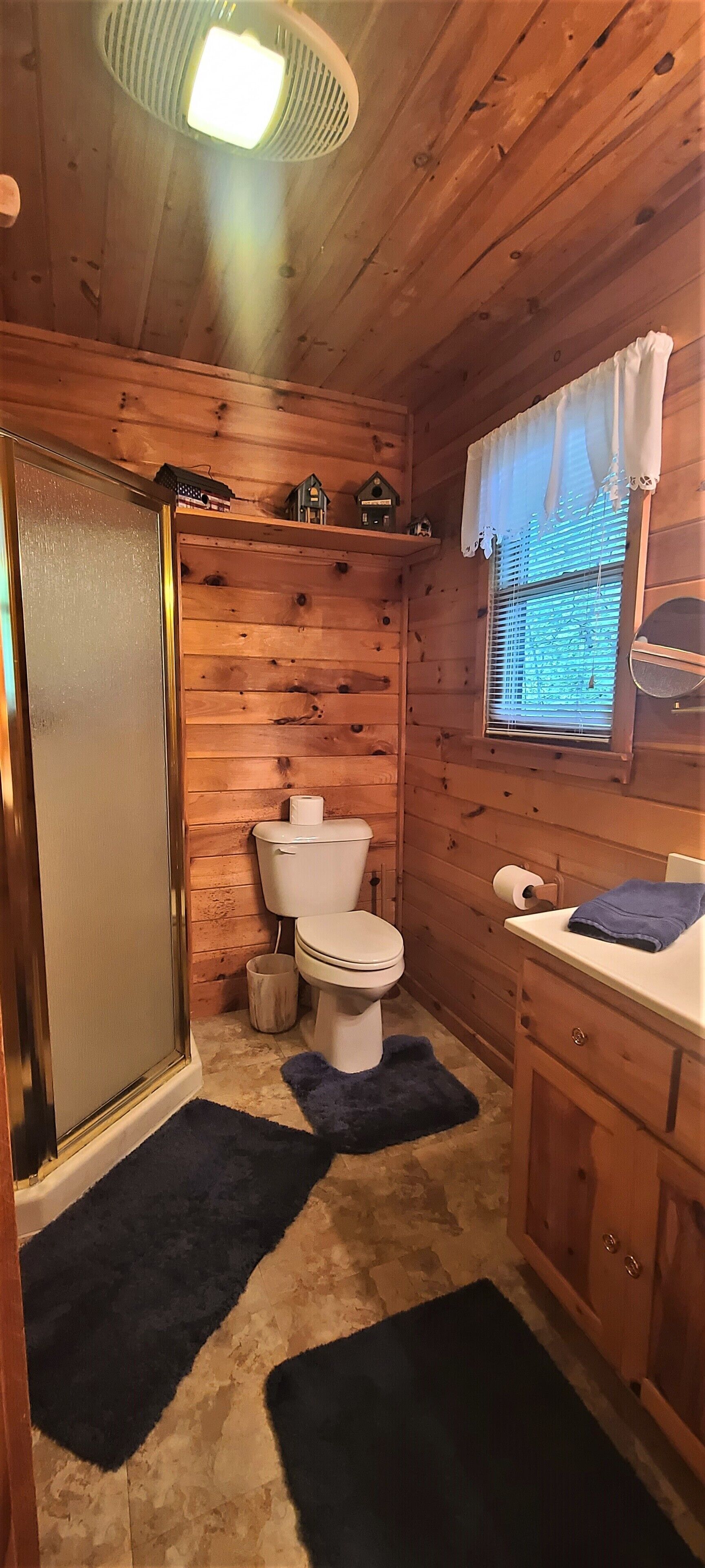 A wooden cabin bathroom with a toilet, sink, and window.
