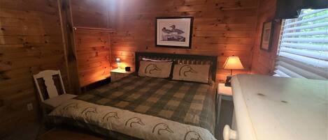 A cozy cabin-style room with a bed, two nightstands, a wooden headboard, and a framed picture on the wall.