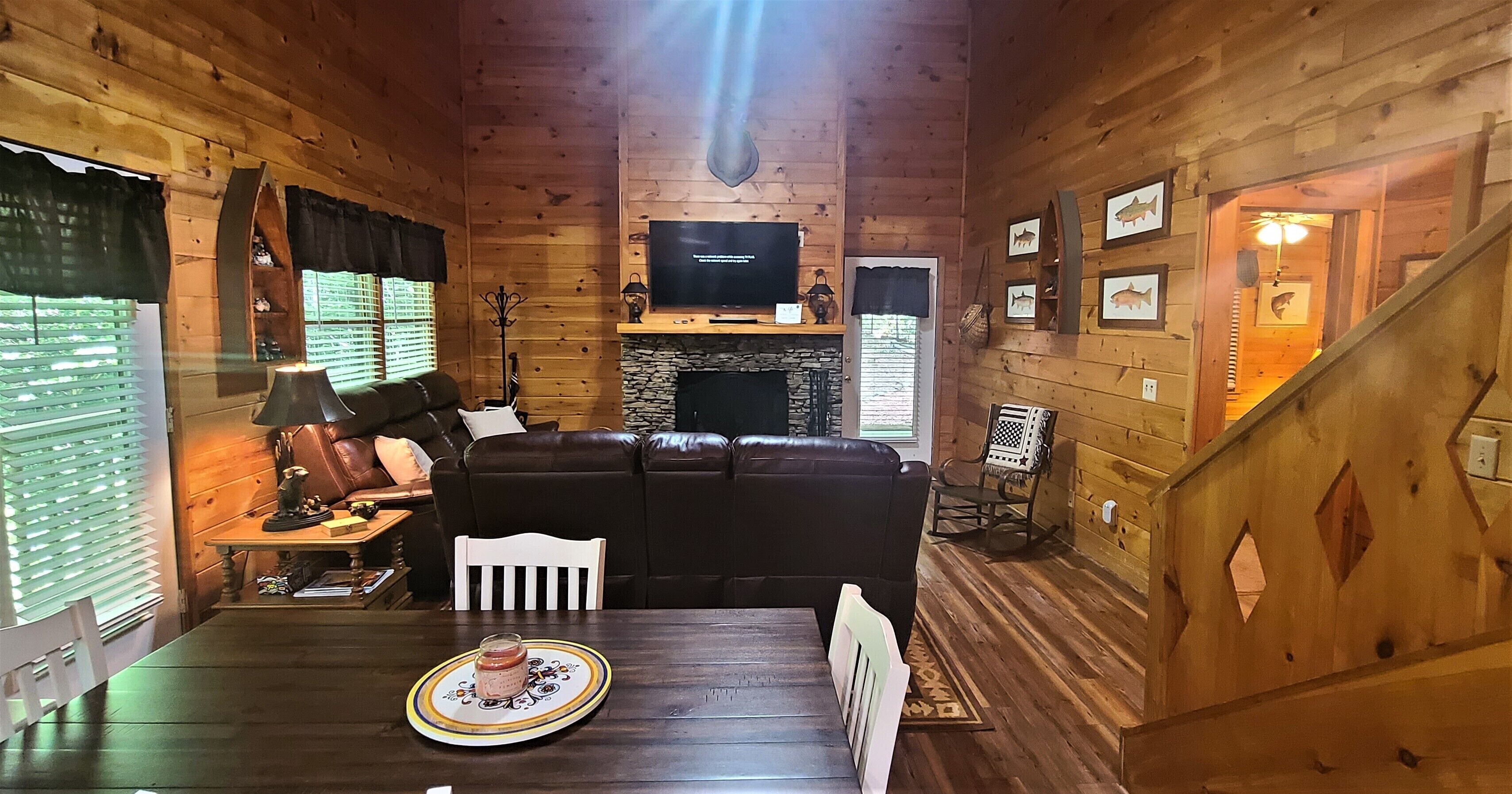 L’intérieur chaleureux d’un chalet, avec un décor en bois, une cheminée, un téléviseur et un coin repas comprenant une table et des chaises.