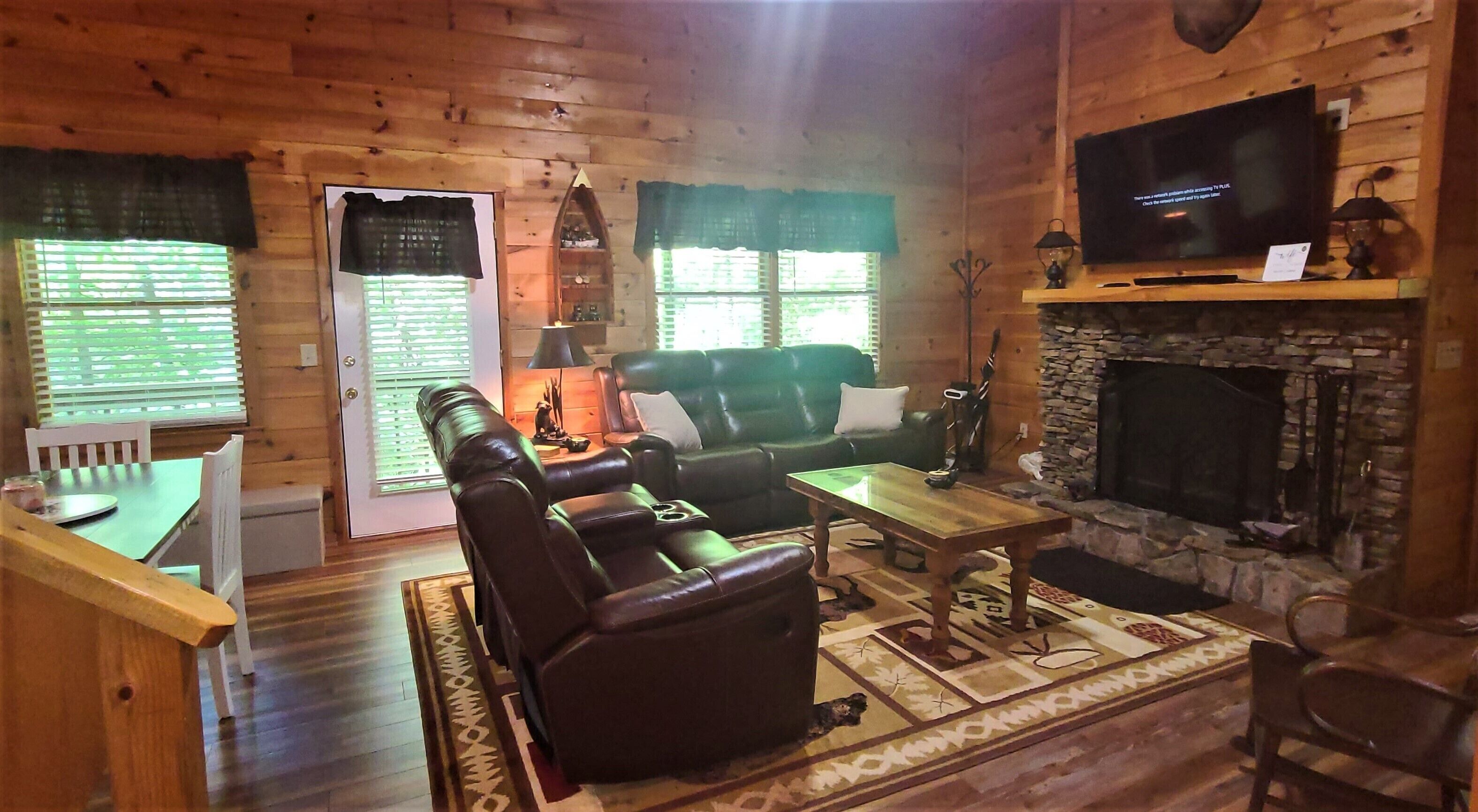 A cozy living room with a fireplace, leather sofa, and a television mounted on the wall.