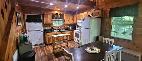 Cocina de cabaña de madera con una mesa de comedor, sillas, refrigerador y un lavamanos.