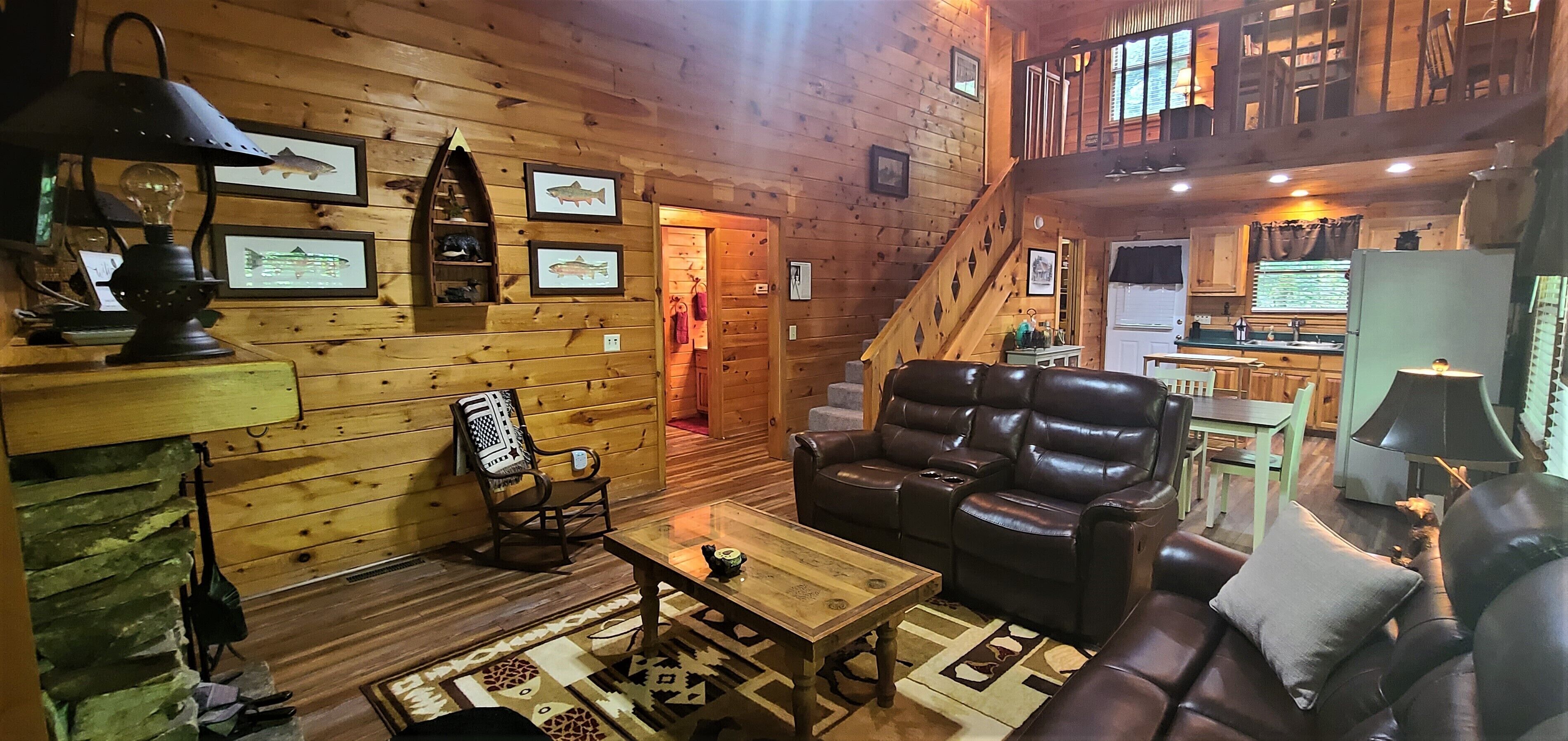 A cozy cabin interior with a wooden interior, a fireplace, leather seating, and framed pictures on the walls.