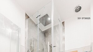 Een moderne badkamer met een douche in glazen cabine, een houten wastafelmeubel, een wit toilet en een backsplash van hexagontegels.