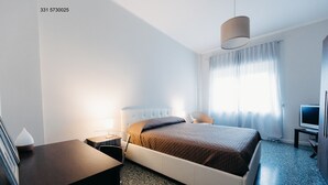 Een moderne hotelkamer met een bed, nachtkastje, lamp, televisie en een bureau met stoel.