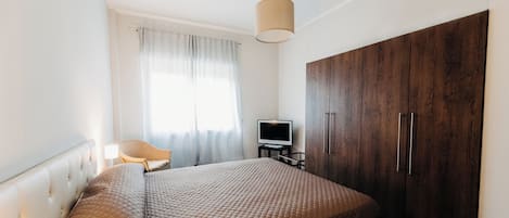 A bedroom with a bed, a television on a stand, a wardrobe, and a chair.