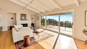 Amplia sala de estar con un sofá blanco, chimenea y un gran ventanal corredizo que da a un balcón con vistas al exterior.