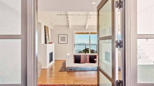 Un interior moderno con suelo de madera, chimenea y vistas al océano a través de amplios ventanales.