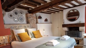A bedroom with a large bed, a brick wall, a fireplace, and a round mirror.