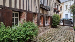 A traditional half-timbered building with a cobblestone courtyard, wooden shutters, and a small garden area.
