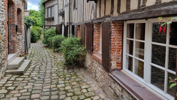 A narrow cobblestone alley flanked by traditional half-timbered buildings with brick walls and white window frames.