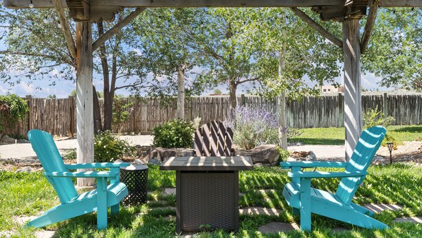 Une terrasse couverte avec deux fauteuils Adirondack turquoise et une table centrale, le tout entouré de verdure et d’une clôture en bois.