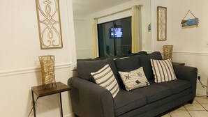Un salon avec un canapé gris foncé, deux coussins à rayures, une table d’appoint en osier et un grand miroir au mur.