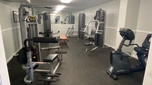 Une salle de sport équipée de divers appareils d’entraînement, notamment un banc de développé couché, un support à squats et un appareil elliptique.