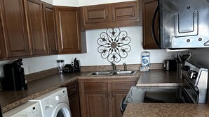Une cuisine compacte avec des meubles en bois, un lave-linge encastré, un four à micro-ondes et un plan de travail en granit.