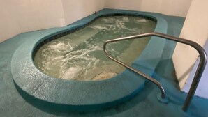 Un bain à remous équipé d’un escalier en métal, entouré de murs recouverts de carreaux aux motifs bleus et blancs.