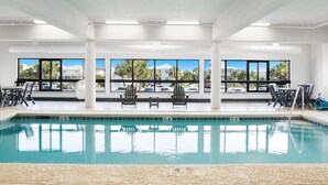 Una piscina con agua cristalina, rodeada de pilares blancos y amplias ventanas que ofrecen vistas a palmeras y edificios.