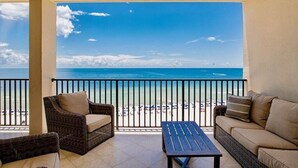 Un balcón con muebles de mimbre, una mesa y vista a la playa y al océano.