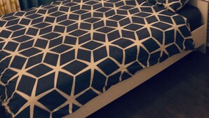 A bed with a geometric patterned bedspread, a headboard with a mirror, and a wall with a leaf-patterned wallpaper. - Entire apartment (Reims)