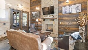 A cozy cabin interior with a stone fireplace, wooden walls, a sofa, a coffee table, and a TV mounted on the wall. - Three Wildflowers Cabin - cozy retreat for up to 6 (Broken Bow)