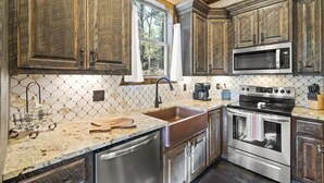 A kitchen with wooden cabinets, a stainless steel dishwasher, a double oven, and a microwave. - Three Wildflowers Cabin - cozy retreat for up to 6 (Broken Bow)