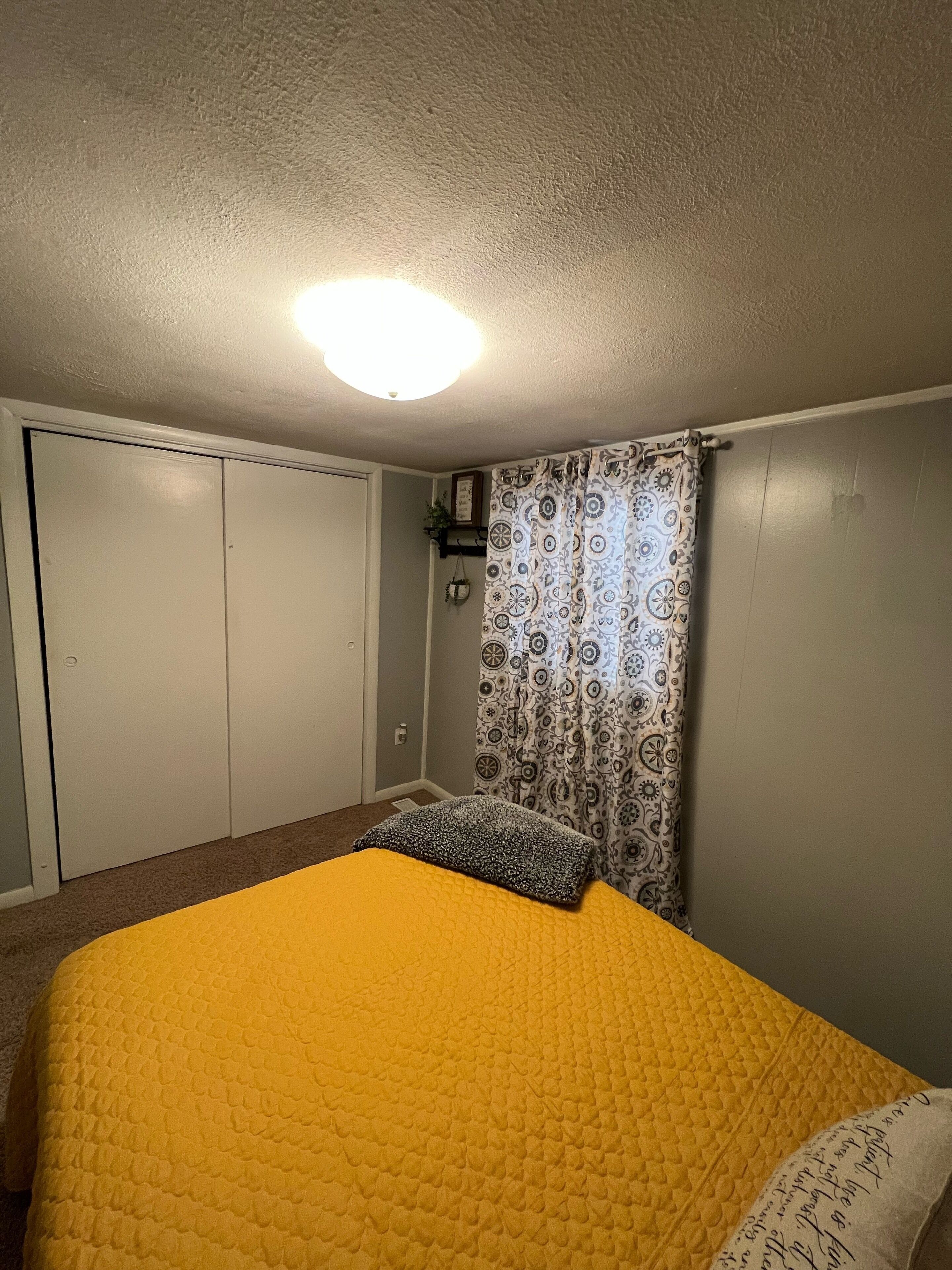 Een slaapkamer met een geel sprei, een patroon gordijn en een plafondlamp.