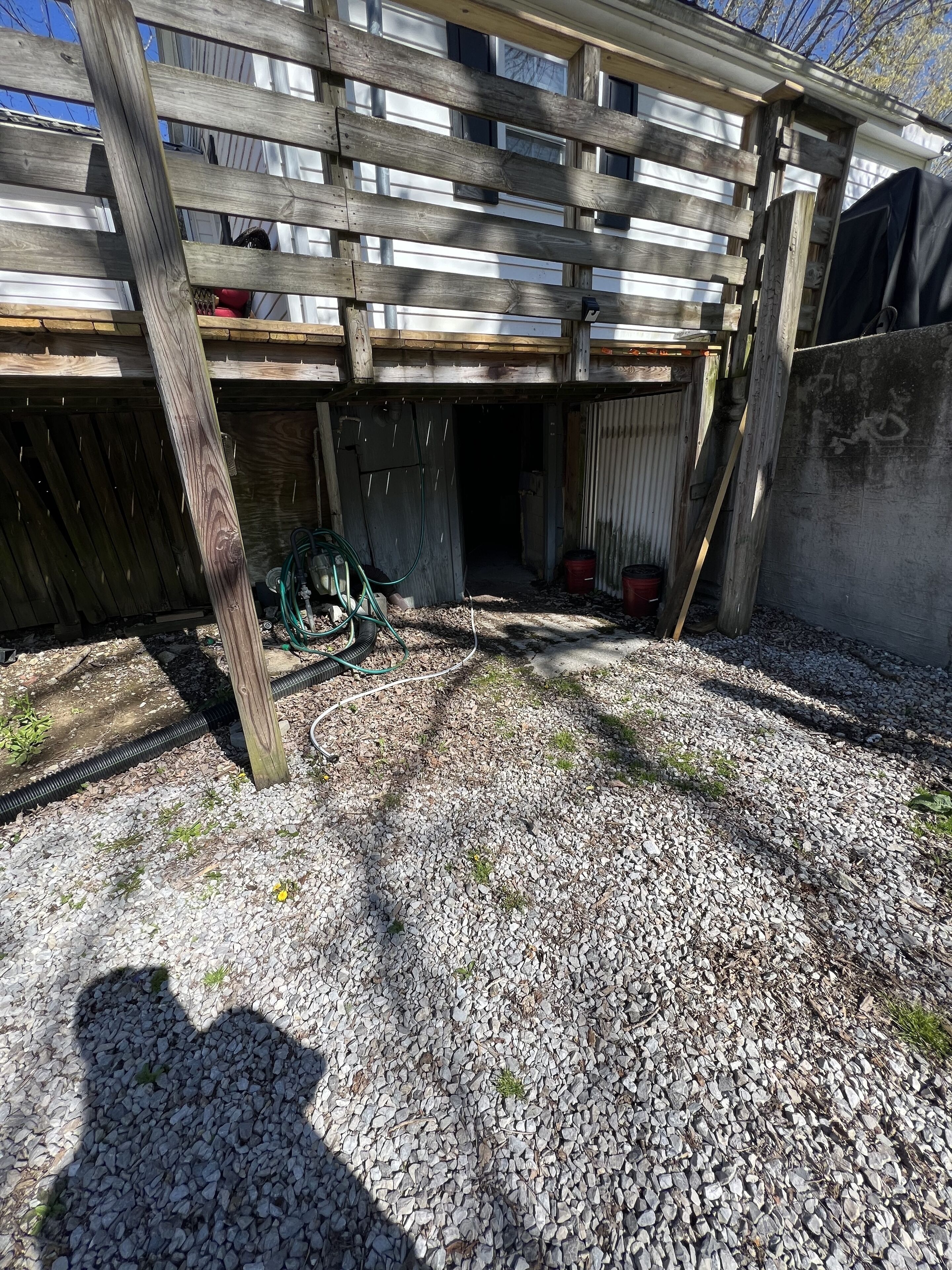 A covered outdoor area with a wooden structure, gravel ground, and a hose.