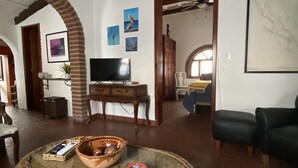 Een woonkamer met een rieten bank, een televisie op een houten dressoir en een groot kunstwerk in een lijst aan de muur.