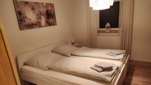 A small, clean room with a single bed, a nightstand, a lamp, and a window with curtains. - Vacation house-Braunlage apartment 2 (Braunlage)