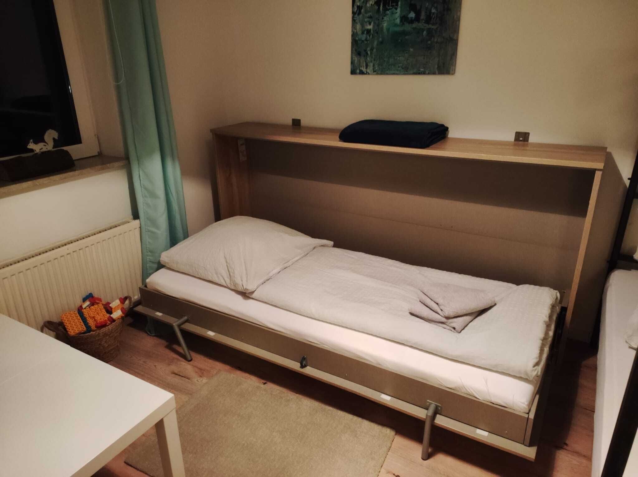 A small, single-bed room with a wooden headboard, a small table, and a radiator.