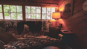 Una habitación acogedora con un sofá estampado, un otoman redondo, una lámpara y un reloj de pared.