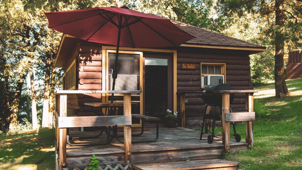 Una cabaña de madera con porche, mesas de picnic y una parrilla.