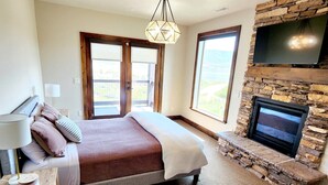 A bedroom with a bed, a TV mounted on a stone wall, and a fireplace. - Luxury Deer Valley East Retreat with Stunning Lake Views - 1.5 miles from slopes (Heber City)