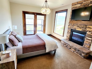 A bedroom with a bed, a TV mounted on a stone wall, and a fireplace.