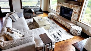Una sala de estar con un sofá, sillones, una mesa de centro, una chimenea y un televisor montado en la pared.