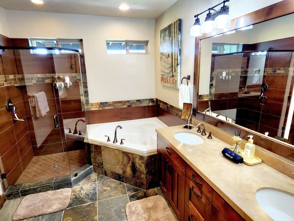 A modern bathroom with a large bathtub, two sinks, a shower area, and a vanity with a mirror.