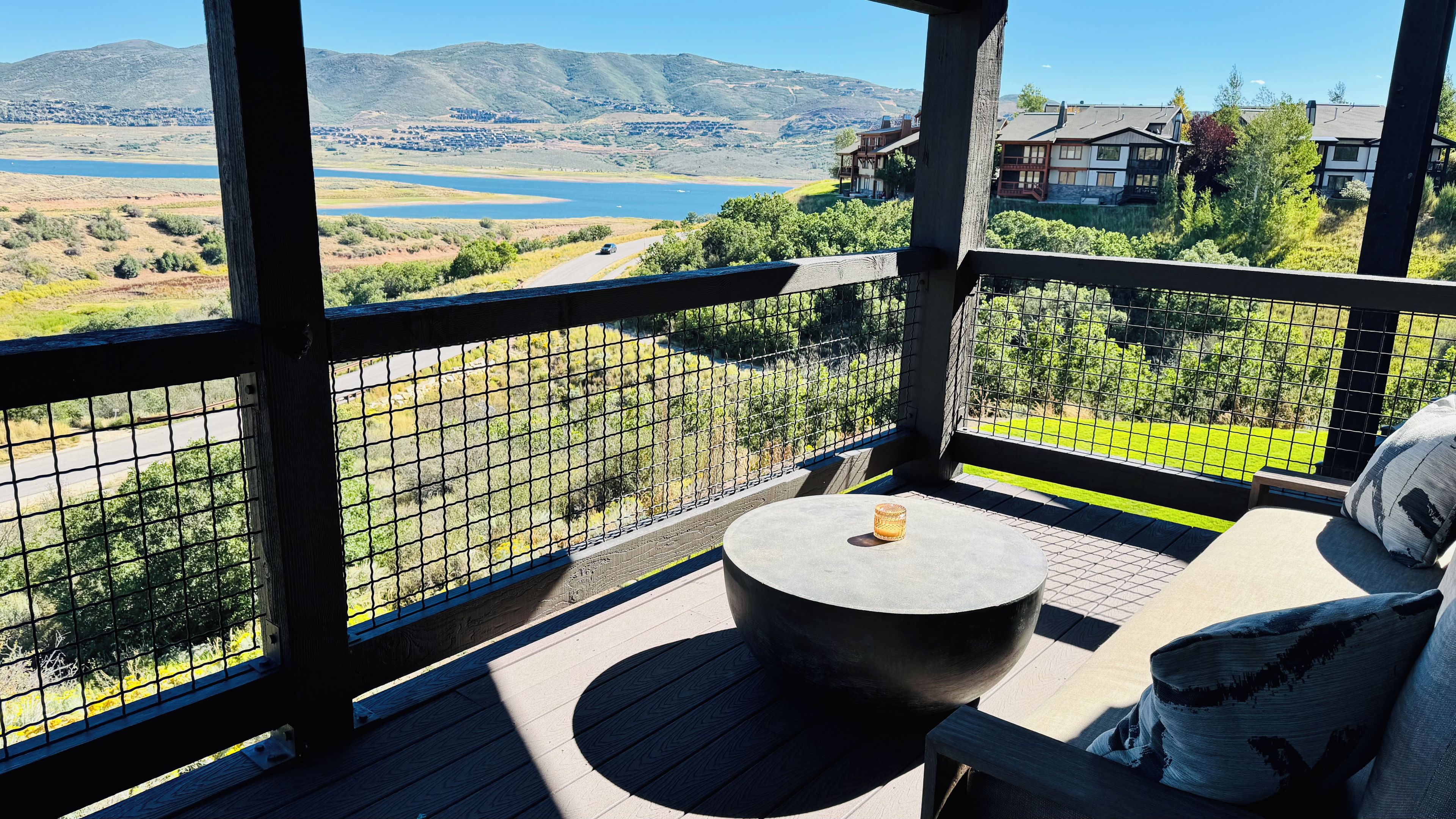Ein Balkon mit Blick auf einen See und Berge, ein runder Tisch und ein Sessel mit Kissen.