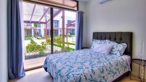 A bedroom with a bed, a window with curtains, a ceiling fan, and an air conditioning unit. - Captivating 2-bed Apartment (Jacó)