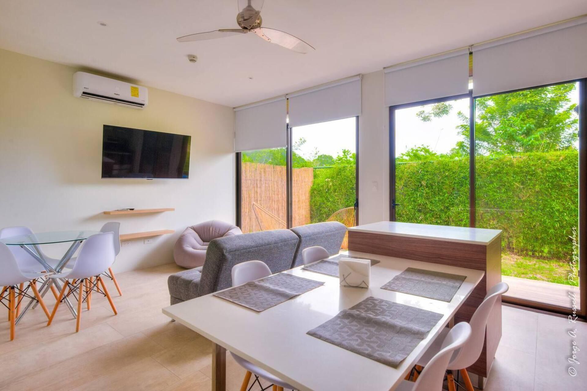 A modern living room with a sofa, a dining table, and a TV mounted on the wall.