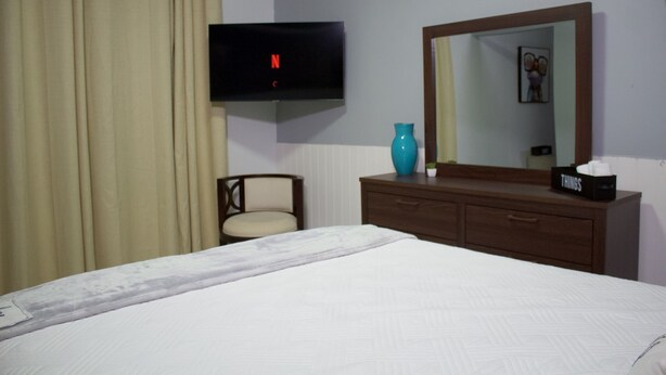 A hotel room with a bed, a TV mounted on the wall, a dresser, a chair, and a mirror.