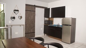 A compact kitchen with a refrigerator, microwave, and black cabinets. There is a dining table with chairs and a sliding door closet.