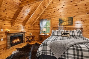 A log cabin bedroom with a fireplace, a bed with plaid bedding, and a wooden ceiling. - Peaceful Smoky Mountain Escape with Stunning Views and Hot Tub (Sevierville)