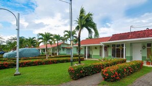 A hotel with a red-tiled roof, green walls, and a well-maintained garden with red flowers and palm trees. - Romantic Tiny Apartment (Jacó)